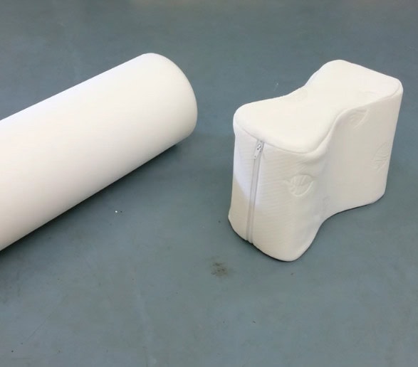 White ergonomic cushion and cylindrical pillow on gray floor.