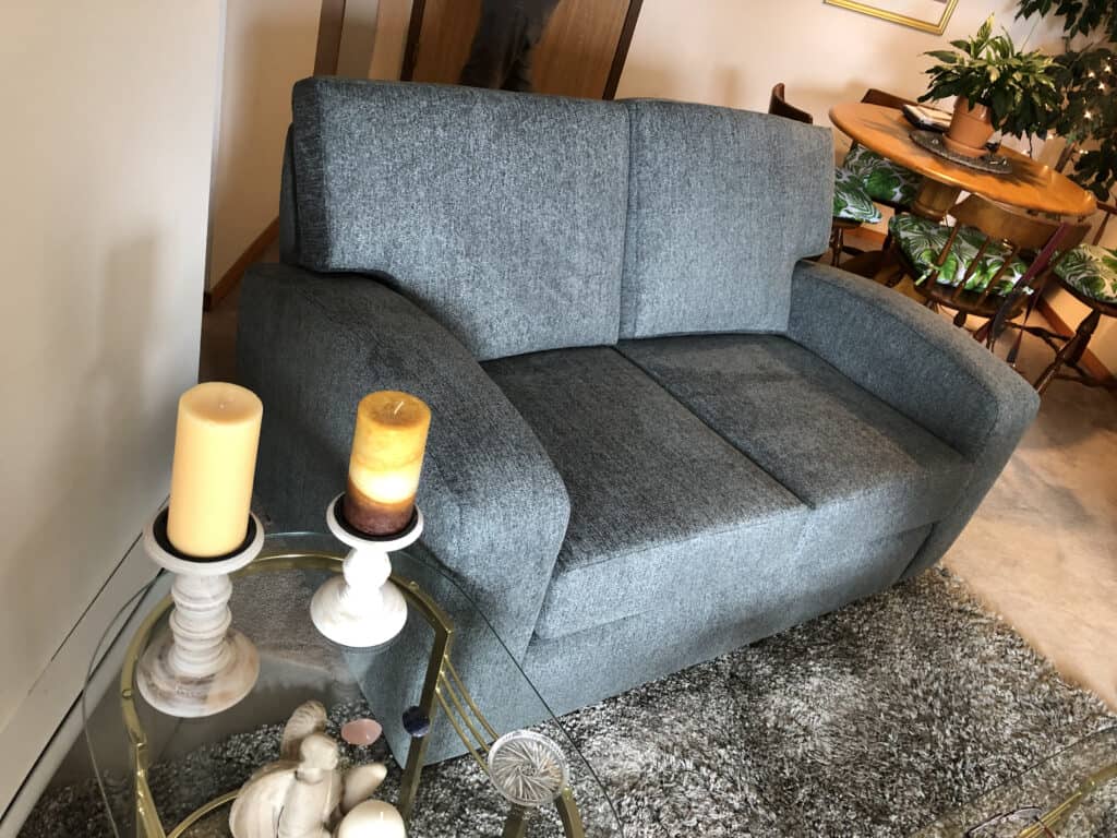 Grey loveseat with candles on side table.