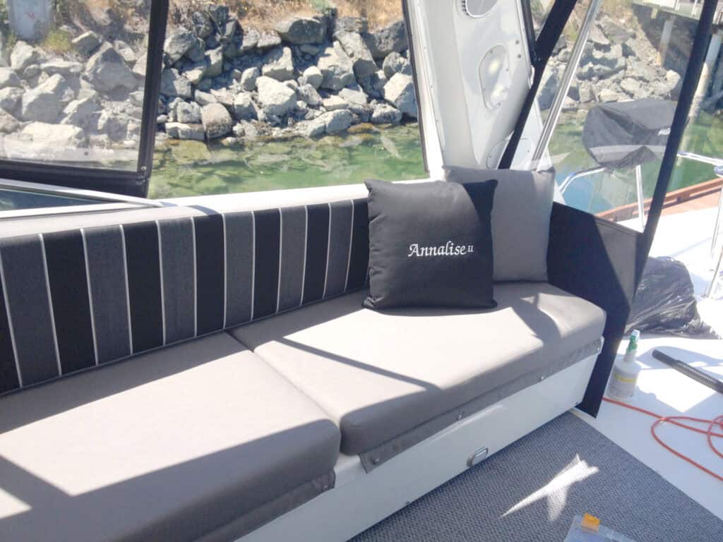 Boat interior with grey seating and embroidered pillow.