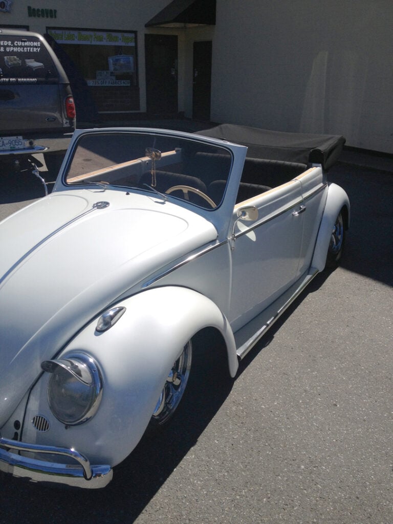 Classic white convertible vintage car parked outside shop.