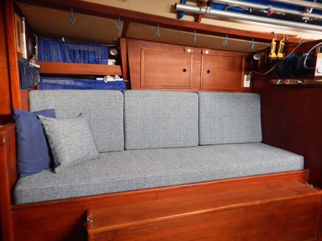 Couch in wooden boat cabin with grey cushions.