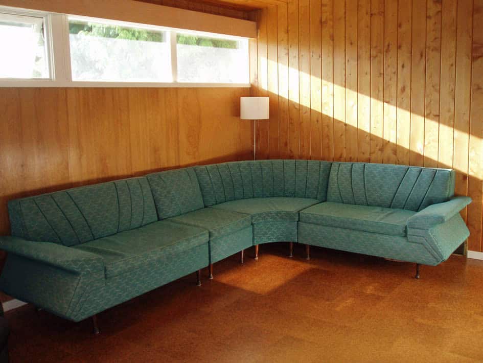 Vintage green sectional sofa in wood-panelled room.