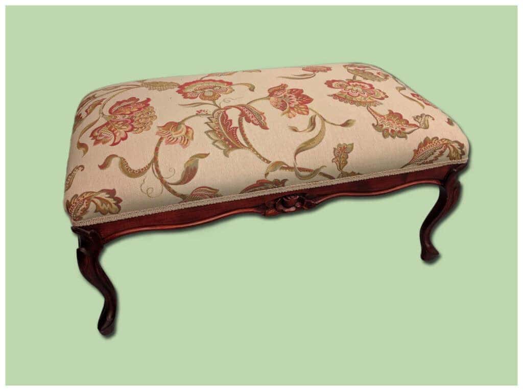 Vintage floral upholstered footstool with carved wooden legs.