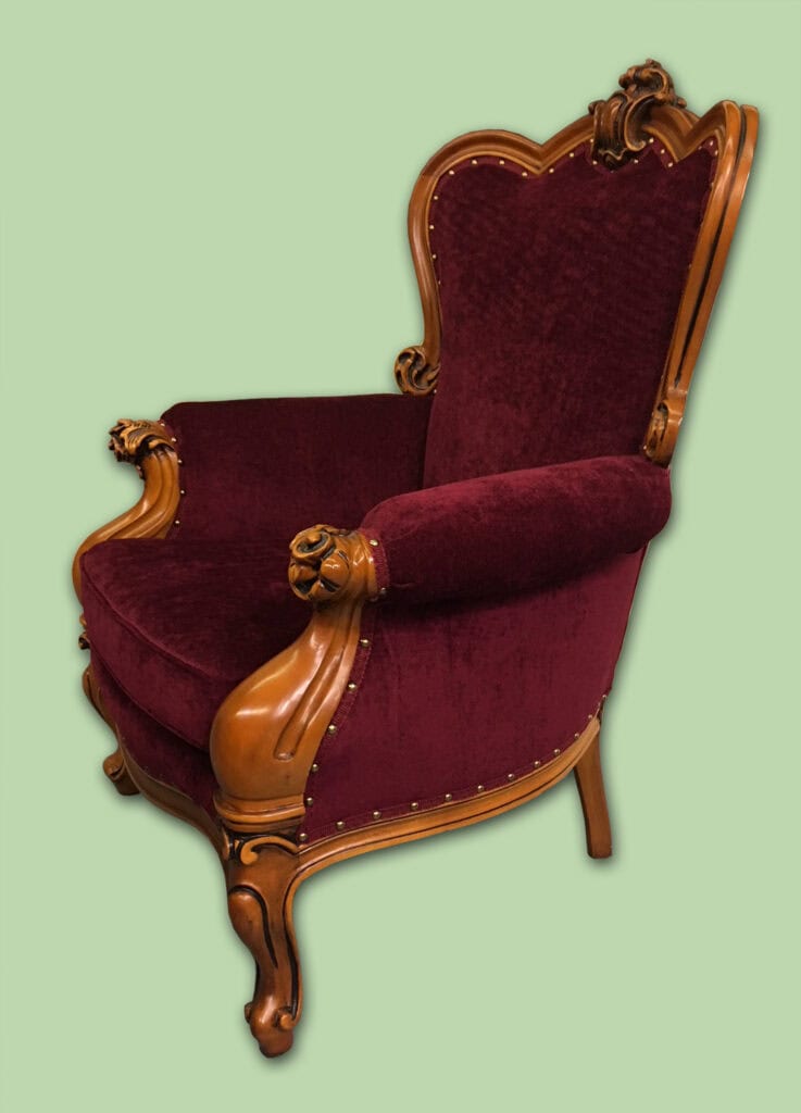 Ornate burgundy velvet armchair with wooden carving.