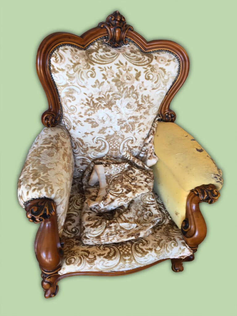 Damaged antique floral armchair on green background.