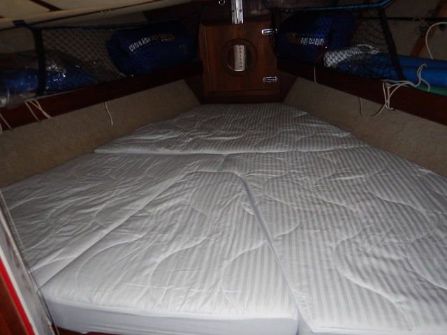 V-berth with white mattresses on a sailboat.